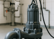 Een robuuste, donkergrijze industriële afvalwaterpomp met leidingen in een betegelde technische ruimte